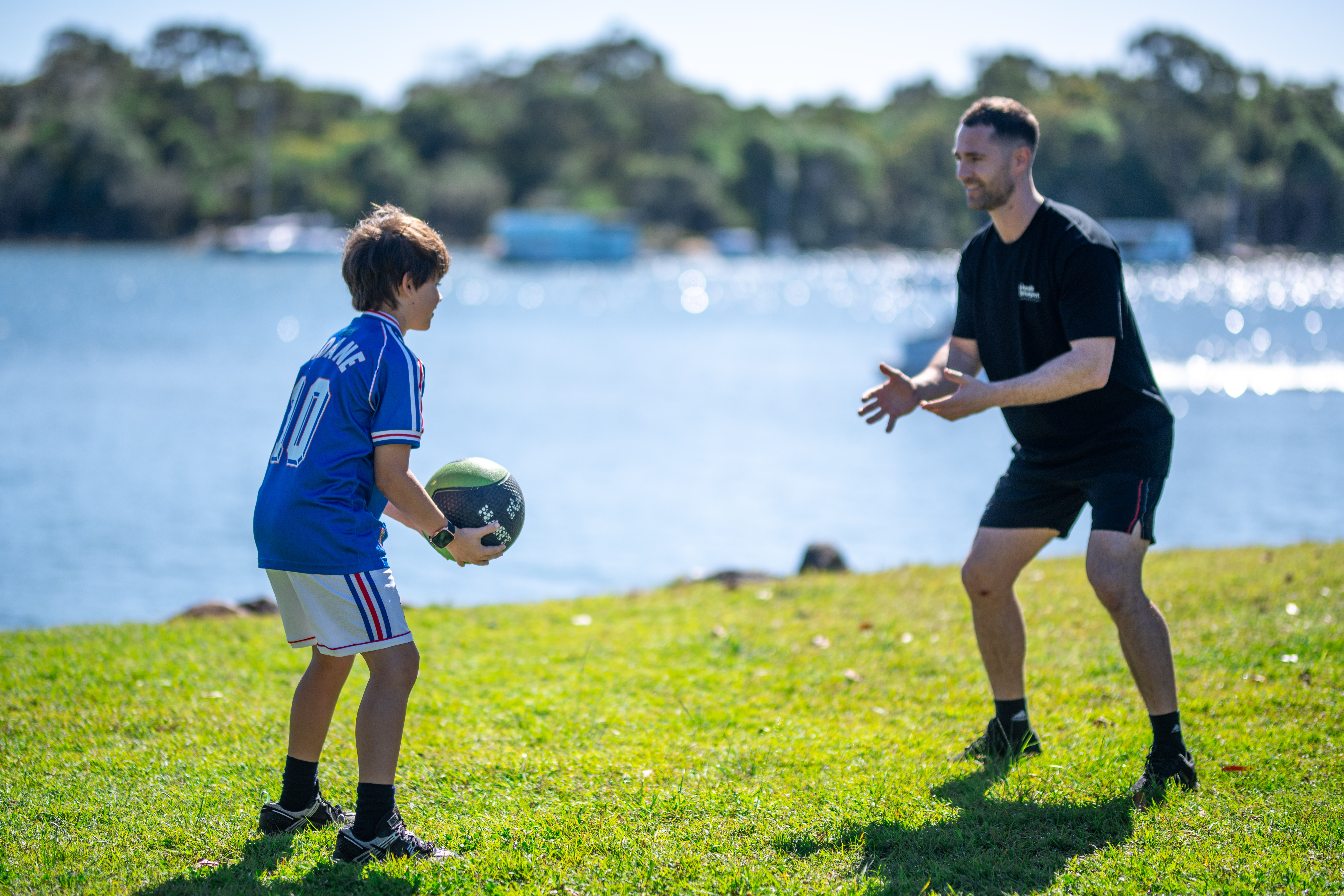 Exercise physiologist working with a child outdoors by the river, practicing ball skills